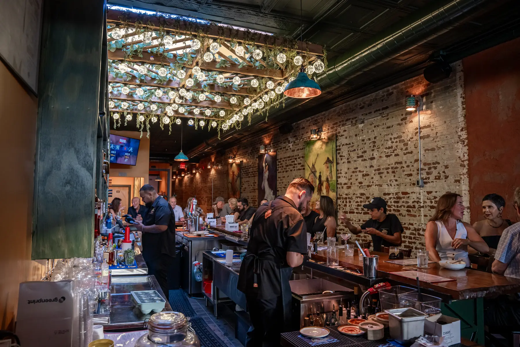 Bartenders working the length of the timber bar while guests sit along it, under strings of filament bulbs hung the full length of the brick room.