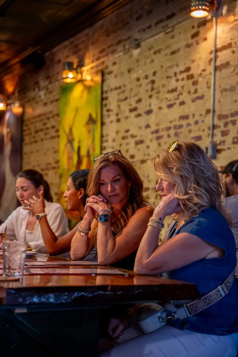 Four guests leaning in around a table against the brick wall, mid-conversation over drinks.