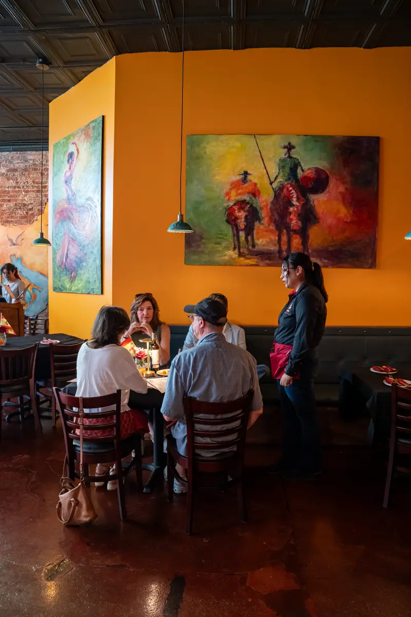 Guests dining beneath a painting of Don Quixote on horseback, hung on a warm ochre wall.